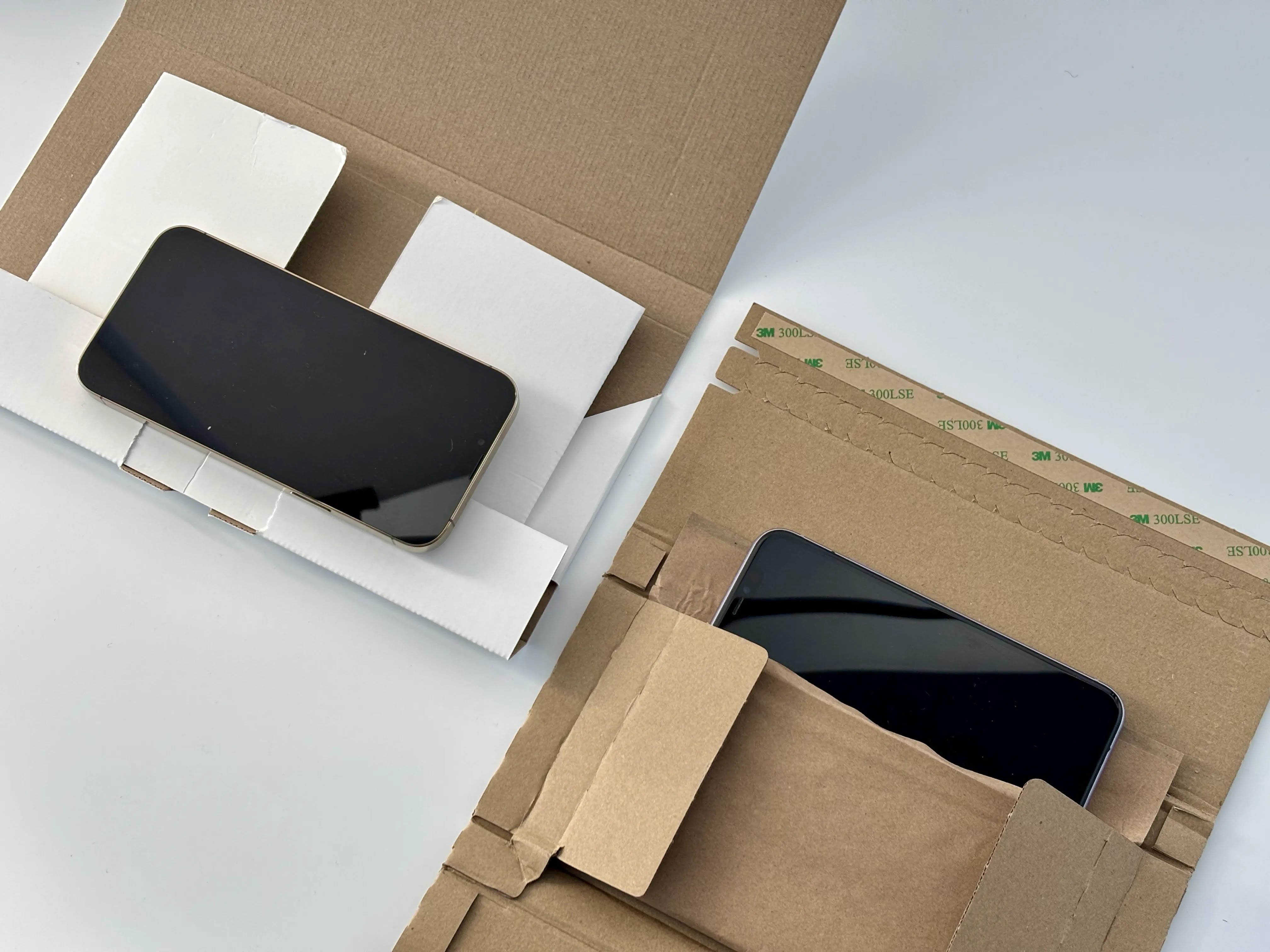 Two open kraft mailer boxes holding smartphones, one in a white cardboard insert and the other in an integrated paper pocket.