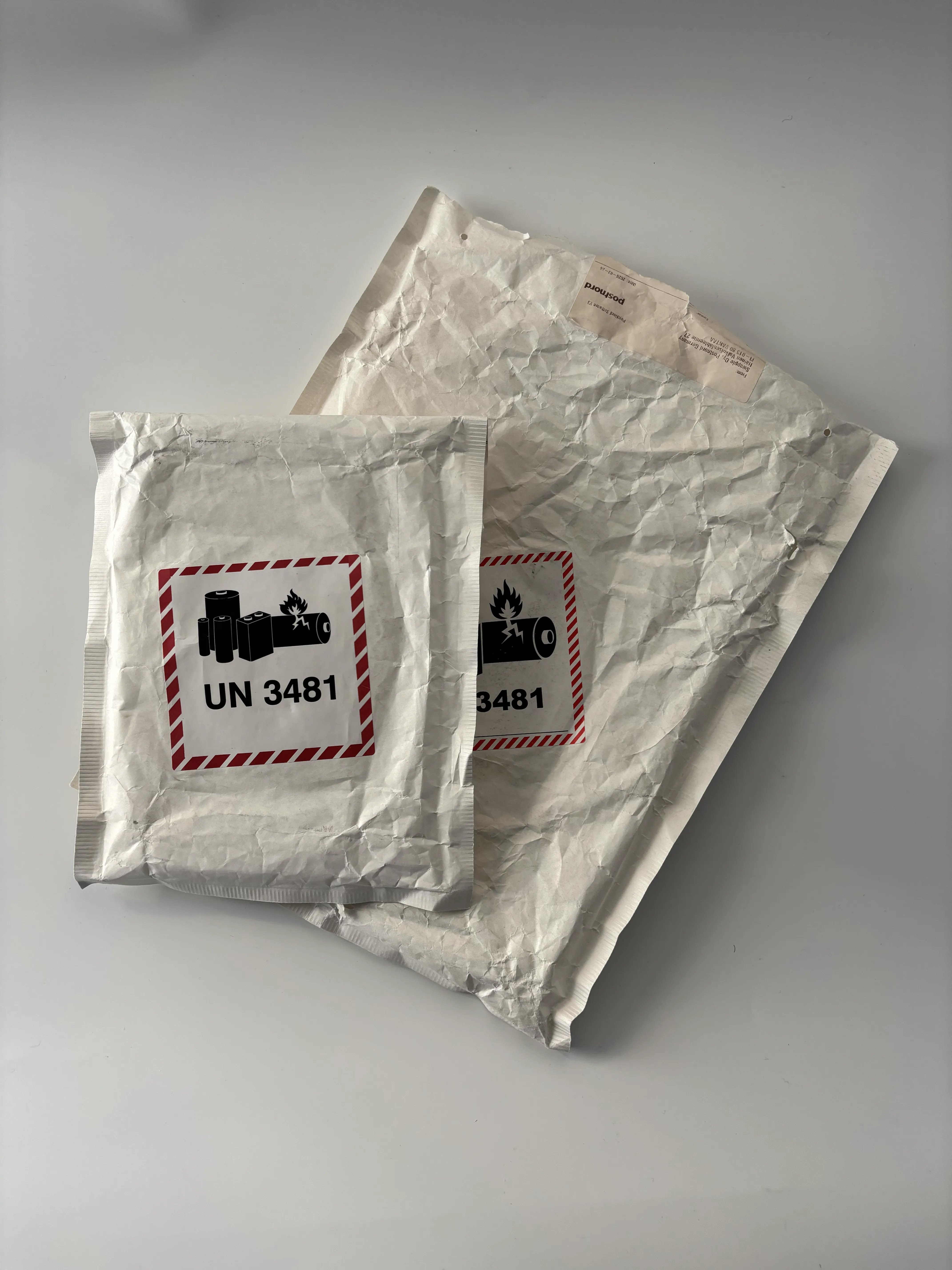 Two overlapping white padded mailers of different sizes, each bearing a UN 3481 battery label.