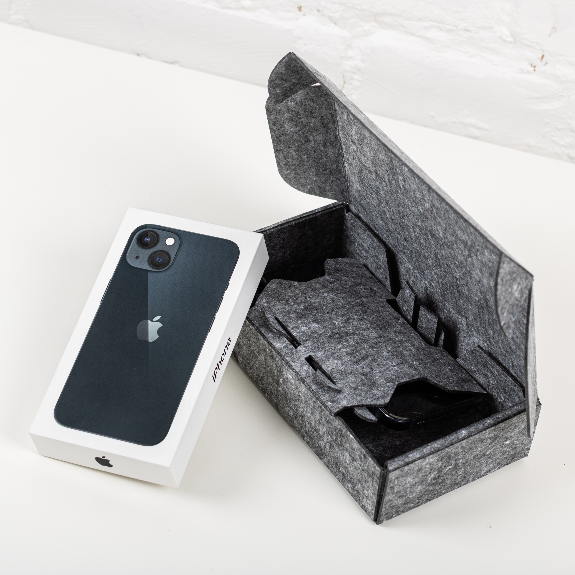 An open grey textile mailer with a fitted inner holder beside a white smartphone retail box.