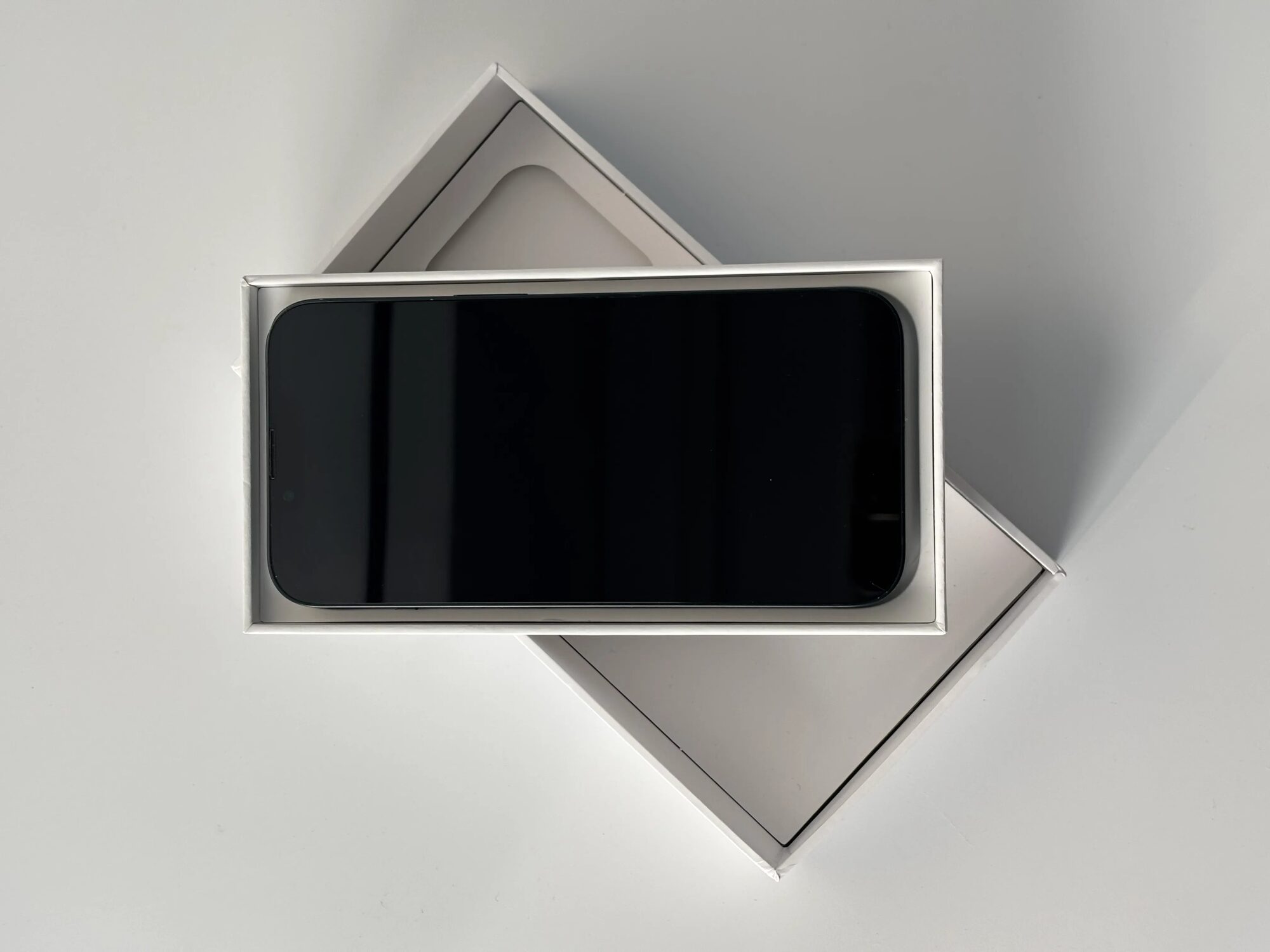 Overhead view of a smartphone in a white two-piece rigid box, with the lid underneath at an angle.